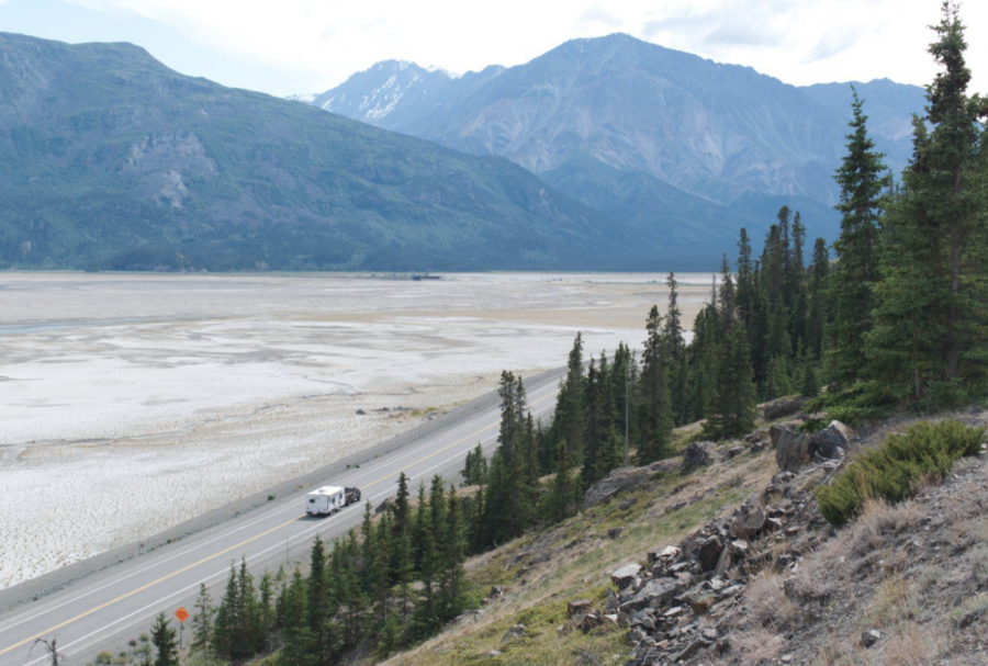 <who> Photo credit: Yukon News </who> A vehicle tugging a trailer cruises down the Alaska Highway on July 21, 2024.