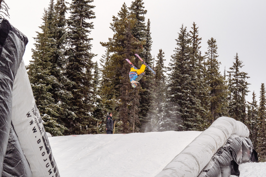 <who>Photo Credit: Benjamin Walker Photography</who>A skier performing an inverted maneuver with a landing airbag below.