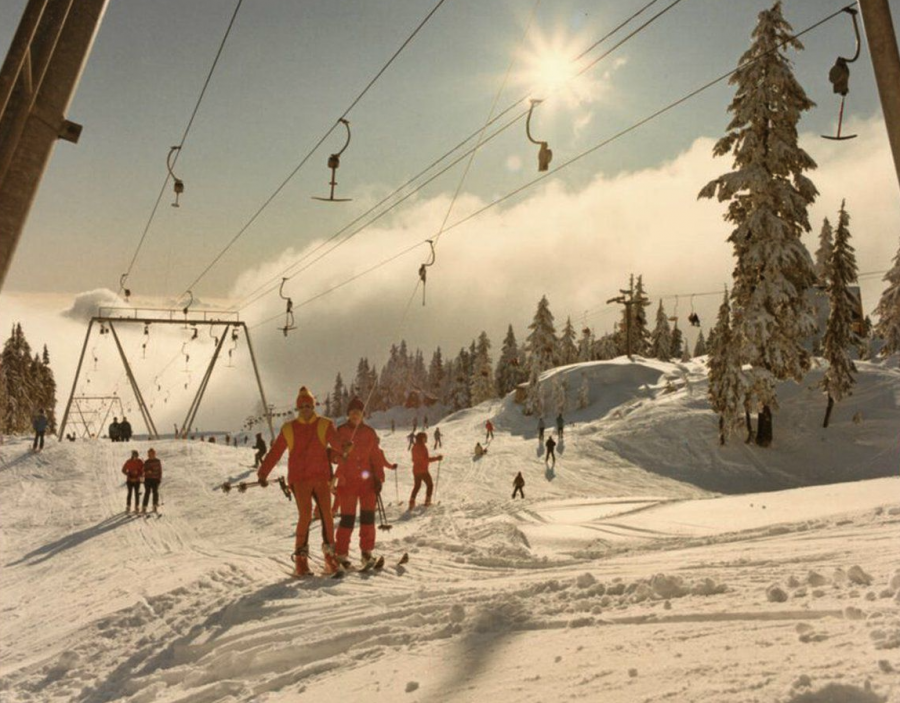 <who> Photo credit: Grouse Mountain </who> Before chairlifts, skiers would ride up Grouse Mountain on T-bars. Skiers would lean against the bar and hold on tight as the system slid them up the hill.