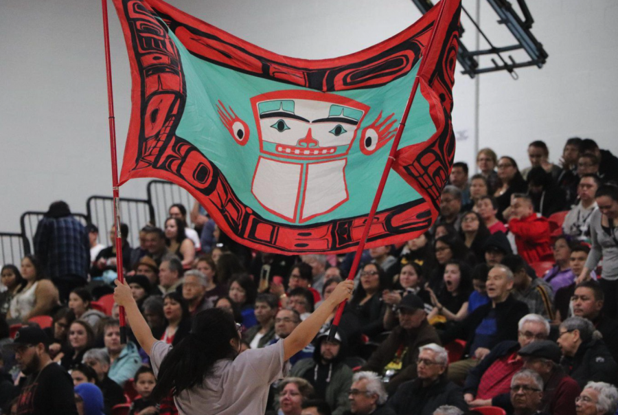 <who> Photo credit: Lax Kw'alaams Band, via Facebook </who> A member of the Lax Kw’alaams Nation waves their band flag during a community gathering in British Columbia.