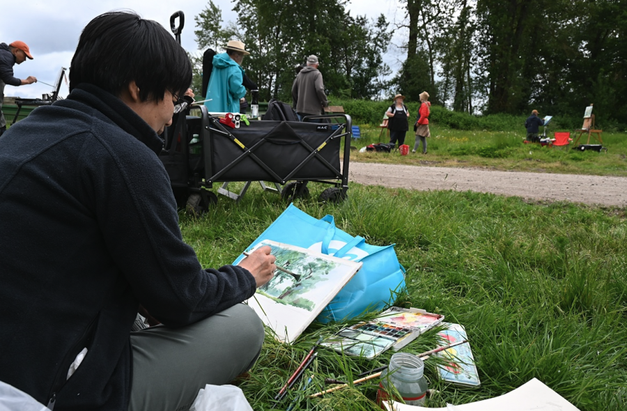 <who> Photo credit: LJI </who> Horae Jiang uses watercolour paints to capture a copse of cottonwood trees at the far end of the grassy field at the Men in Hats meetup.